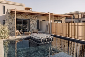 A modern outdoor pool area with stone walls, wooden pergola, and lounge chairs.