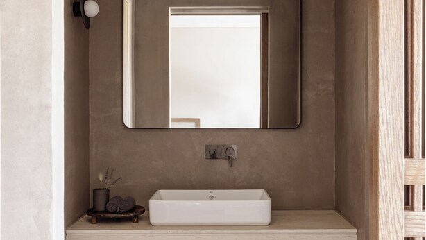 A modern bathroom with a rectangular sink, a mirror above it, and a small shelf with towels and a plant. - Unda (Corfu)