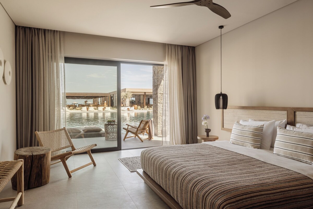 A hotel room with a large bed, a view of a pool and outdoor area, and a ceiling fan.