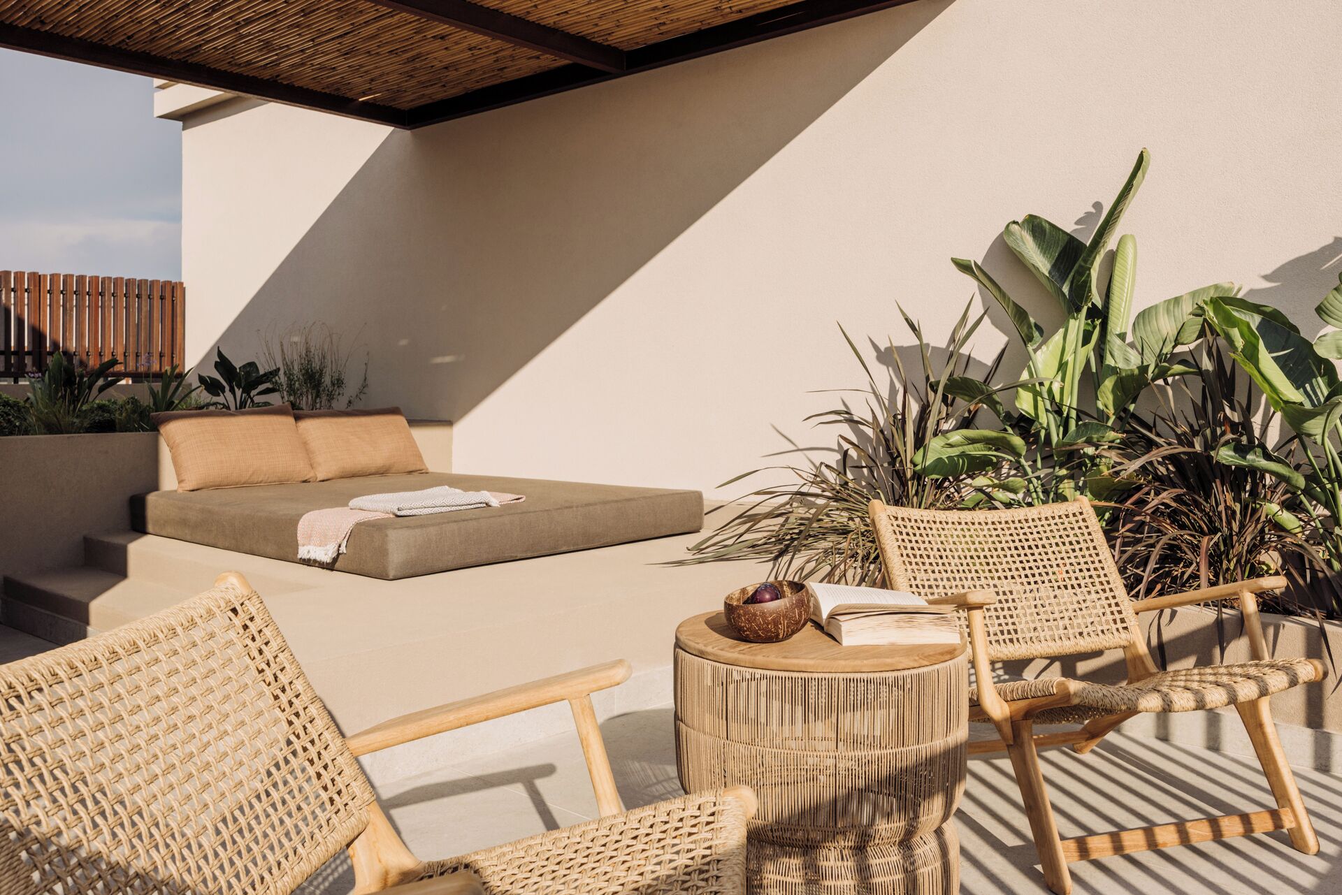 A sunlit outdoor seating area with a sofa, two wicker chairs, and a round table.