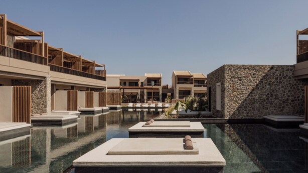A modern resort with a central swimming pool, multiple buildings with balconies, and stone walls.