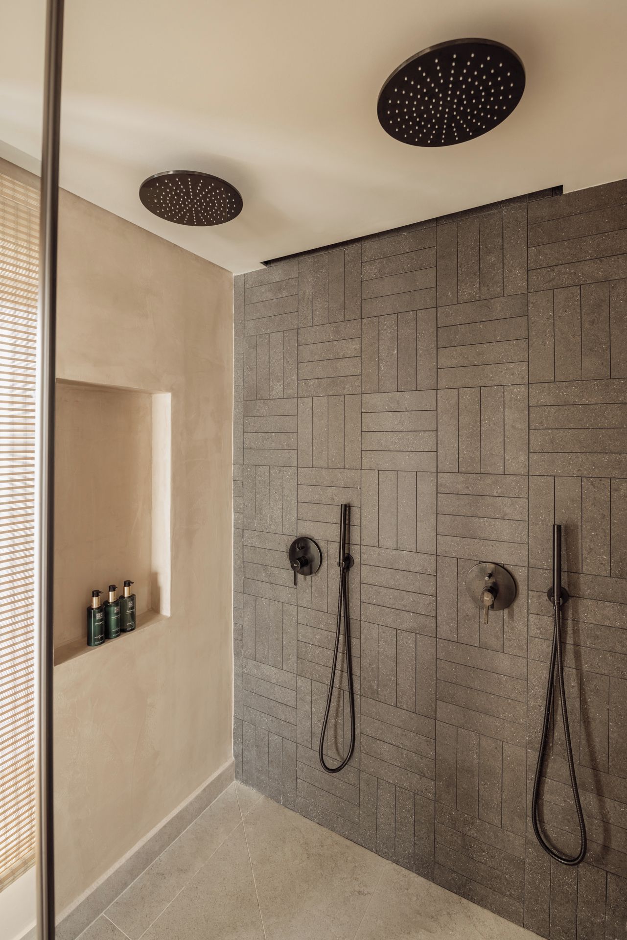 A modern bathroom with a shower area featuring a textured wall, a glass-enclosed shower, and a shelf with toiletries.