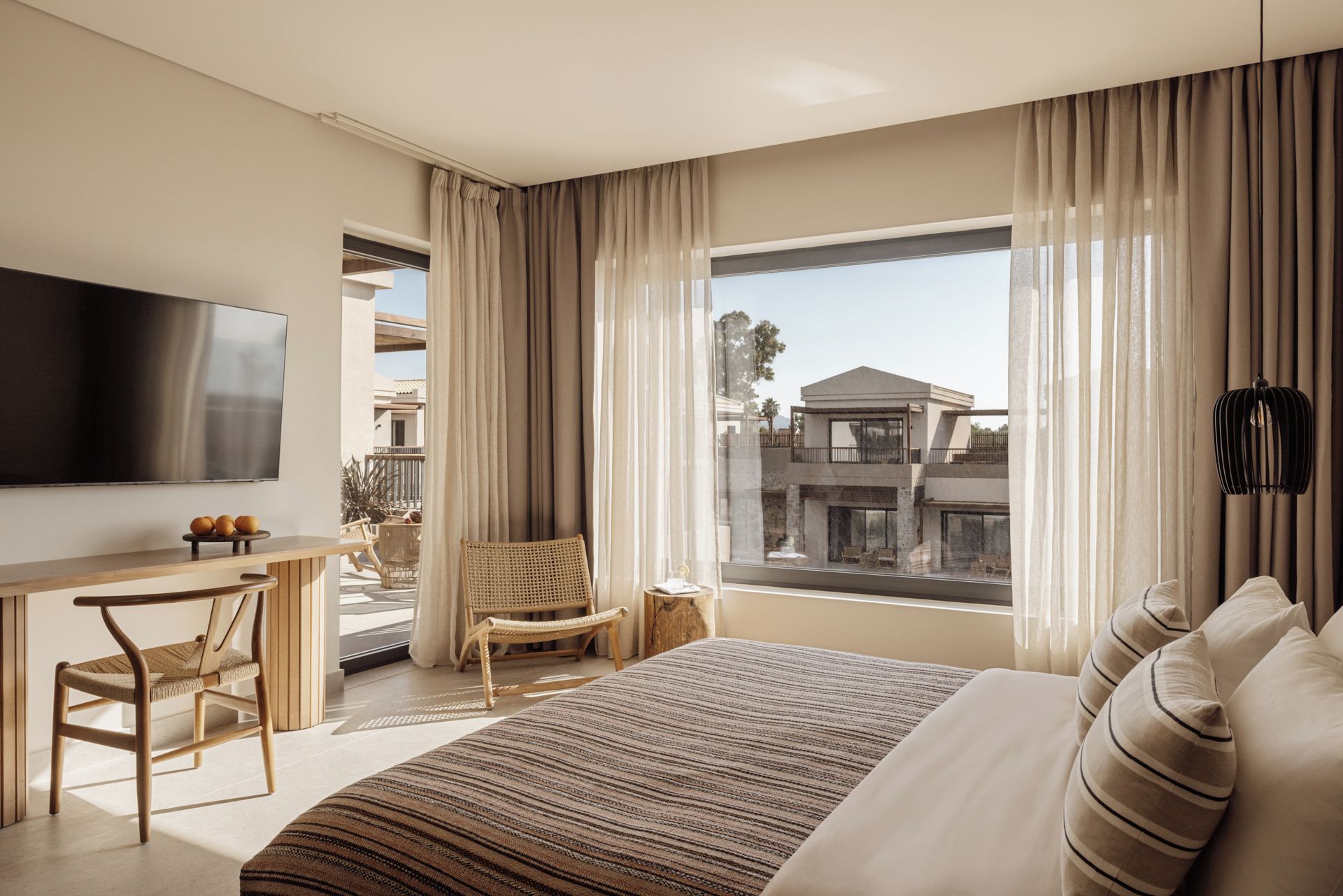 A modern hotel room with a large bed, a flat-screen TV, a desk, and a chair.