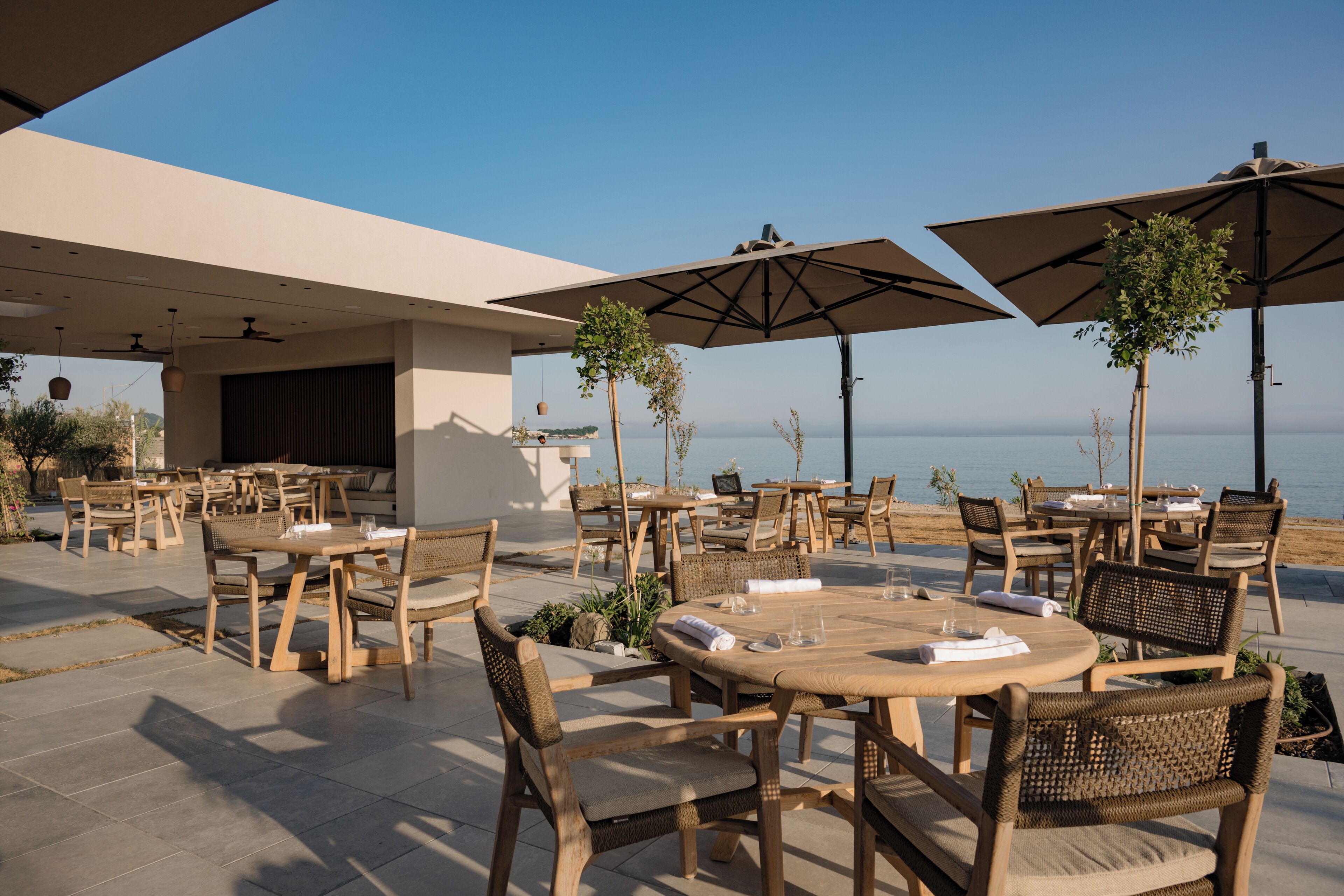 An outdoor seating area with tables and chairs, umbrellas, and a view of the sea.