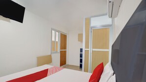Habitación de hotel con cama, ventana, puerta y equipo de aire acondicionado.