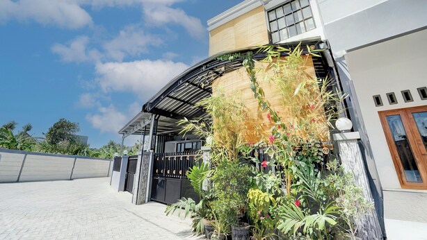 Un edificio moderno con una entrada curva, un porche cubierto y una variedad de plantas y flores en macetas.