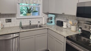 Una cocina moderna con encimera de granito, electrodomésticos de acero inoxidable y una ventana con plantas en macetas.
