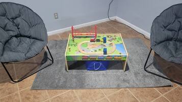 A small play area with a train set table, two chairs, and a grey rug on a tiled floor.