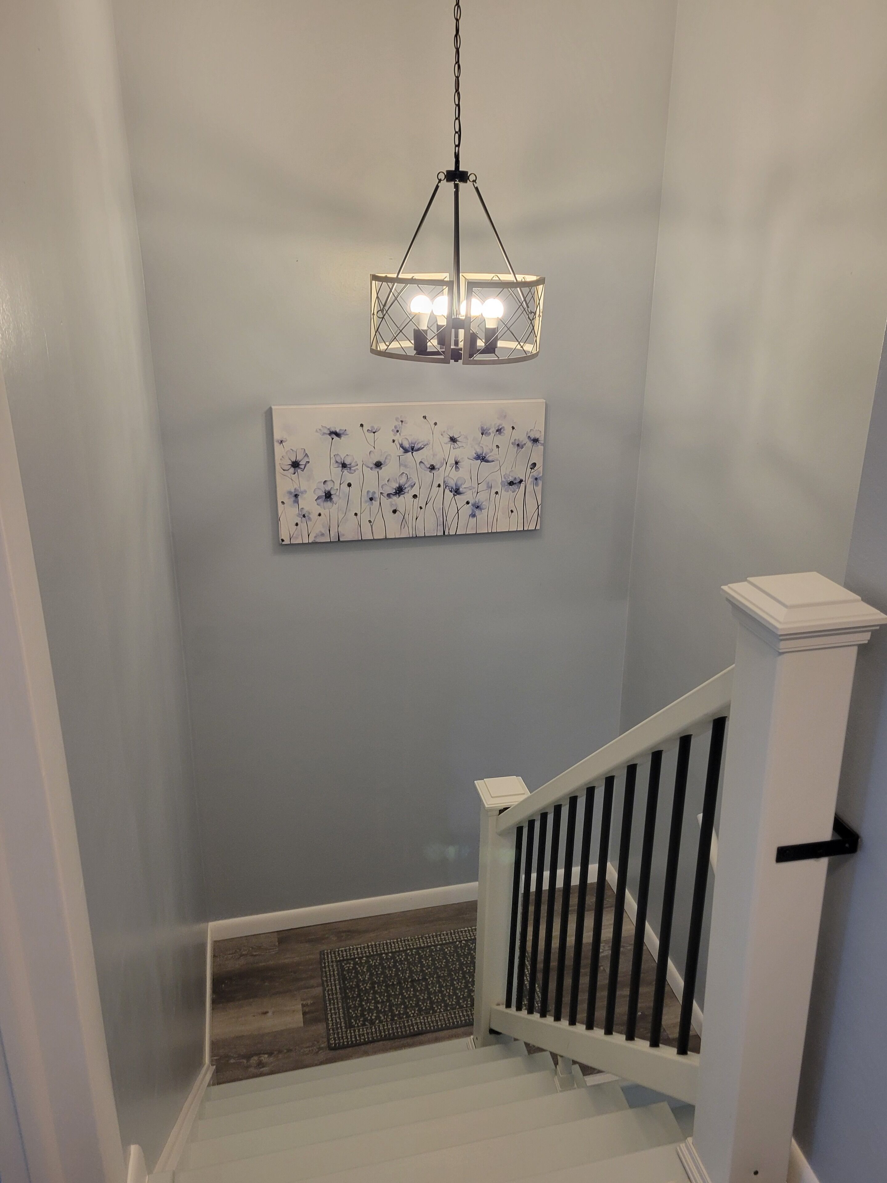 A staircase with a white railing, a wall-mounted light fixture, and a floral artwork.