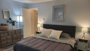 Un dormitorio con cama, cómoda, mesitas de noche y una puerta que da a otra habitación.