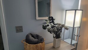 Una habitación con pared gris, un espejo, una cesta tejida y un florero con flores.