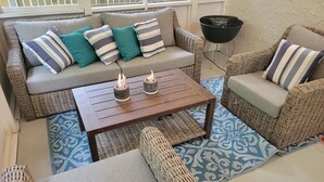 Un rincón exterior acogedor con muebles de mimbre, una mesa de madera y dos velas.