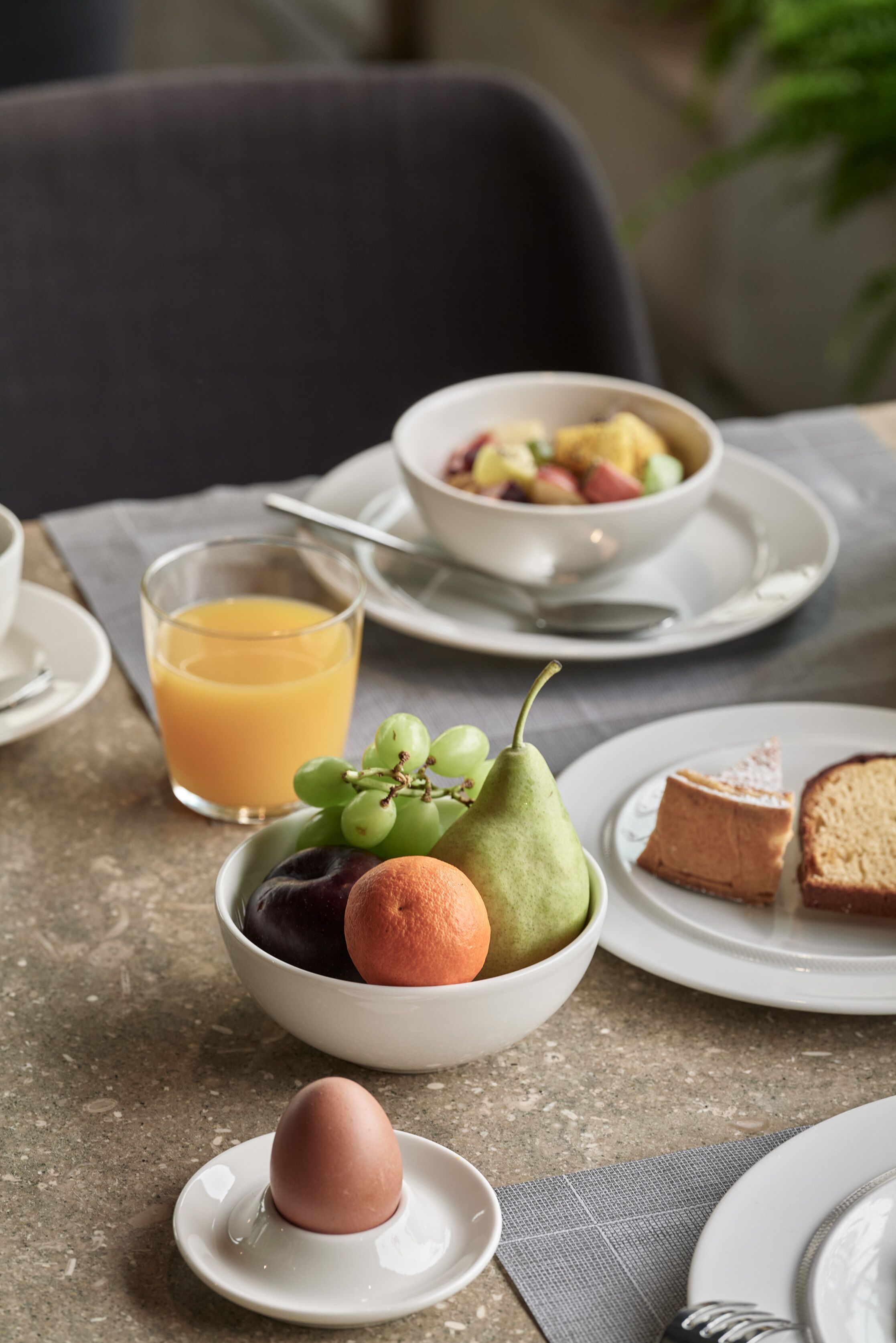 Un desayuno con un tazón de fruta, un vaso de jugo de naranja y un plato con tostadas y una rebanada de pastel.