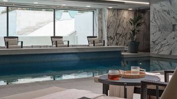 Área de piscina interna com assentos e uma mesa com bebida.