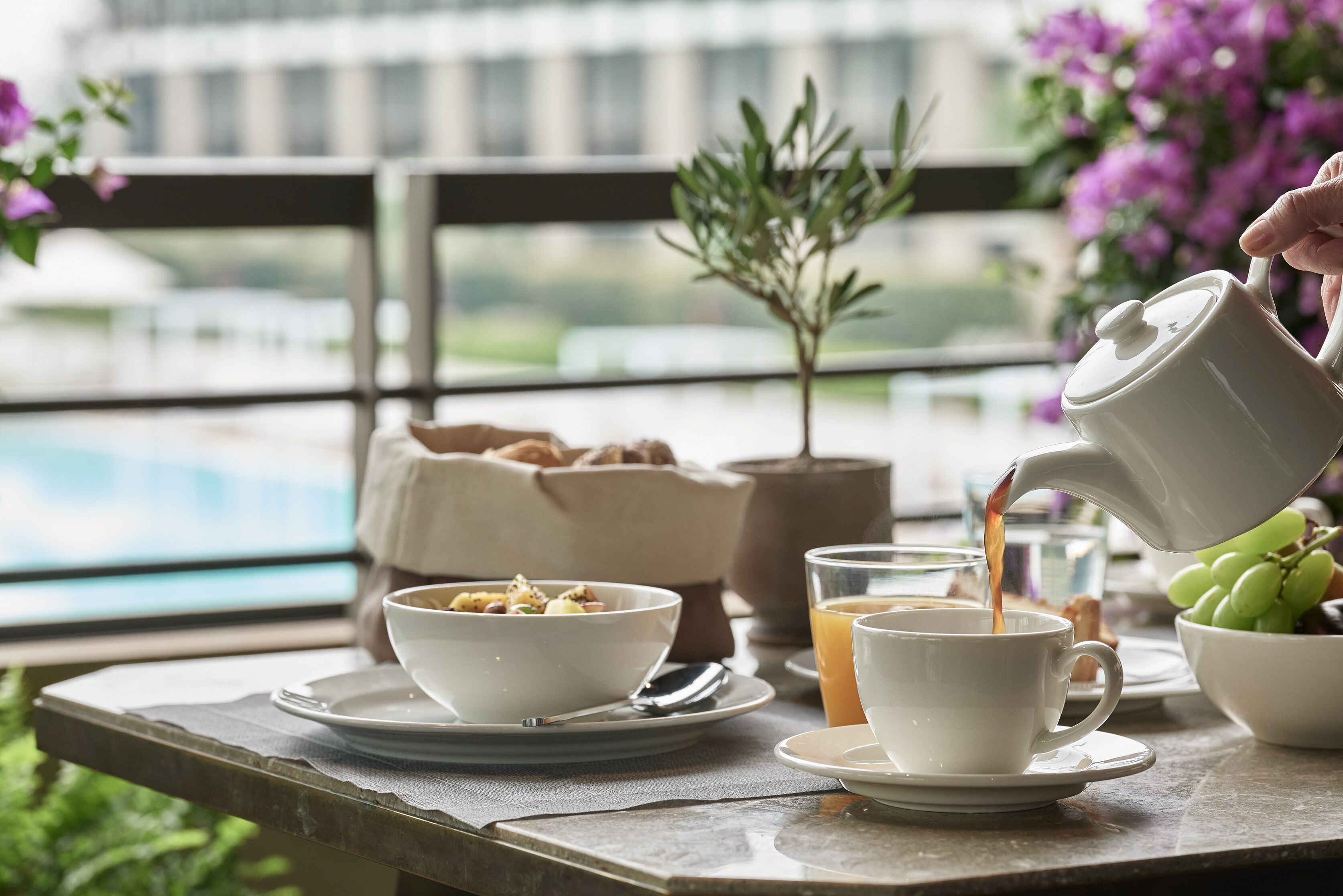 Une table mise pour le petit-déjeuner, avec un bol de céréales, une tasse de café et une carafe dont on verse le contenu dans une tasse.