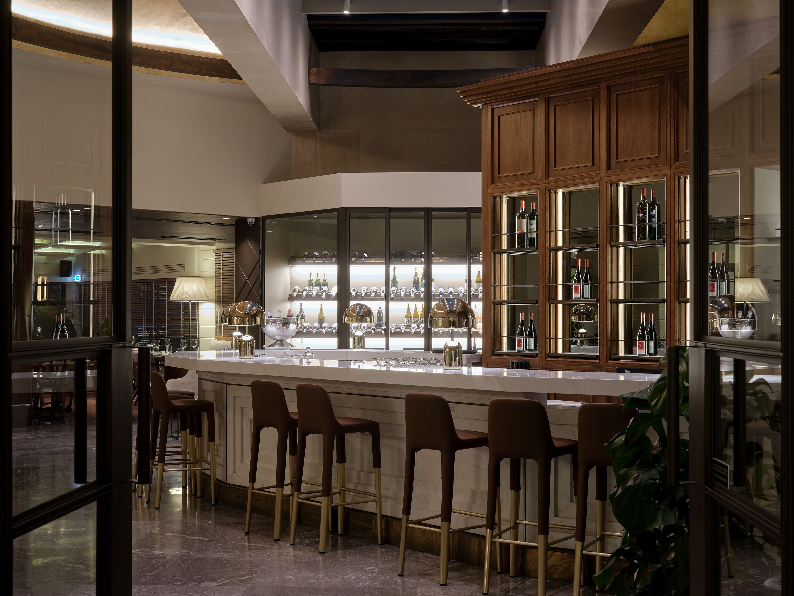 A modern bar area with a marble countertop, bar stools, and a wine display cabinet.