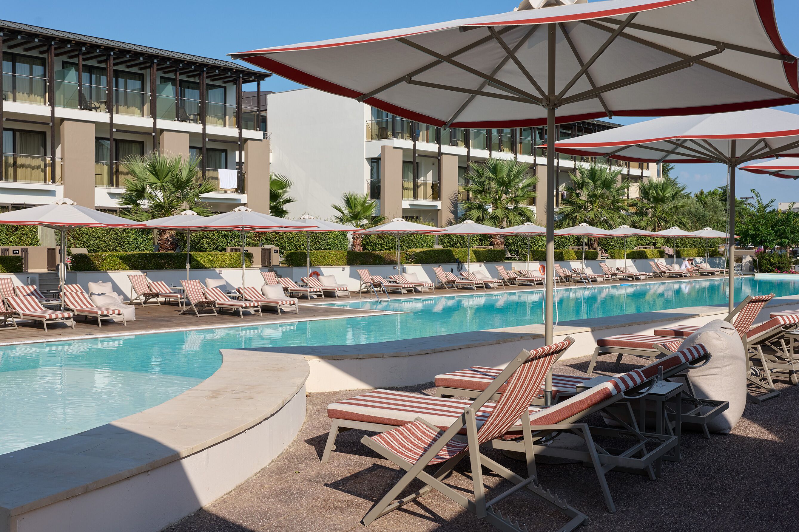 A swimming pool with lounge chairs and umbrellas, surrounded by a modern building with balconies.