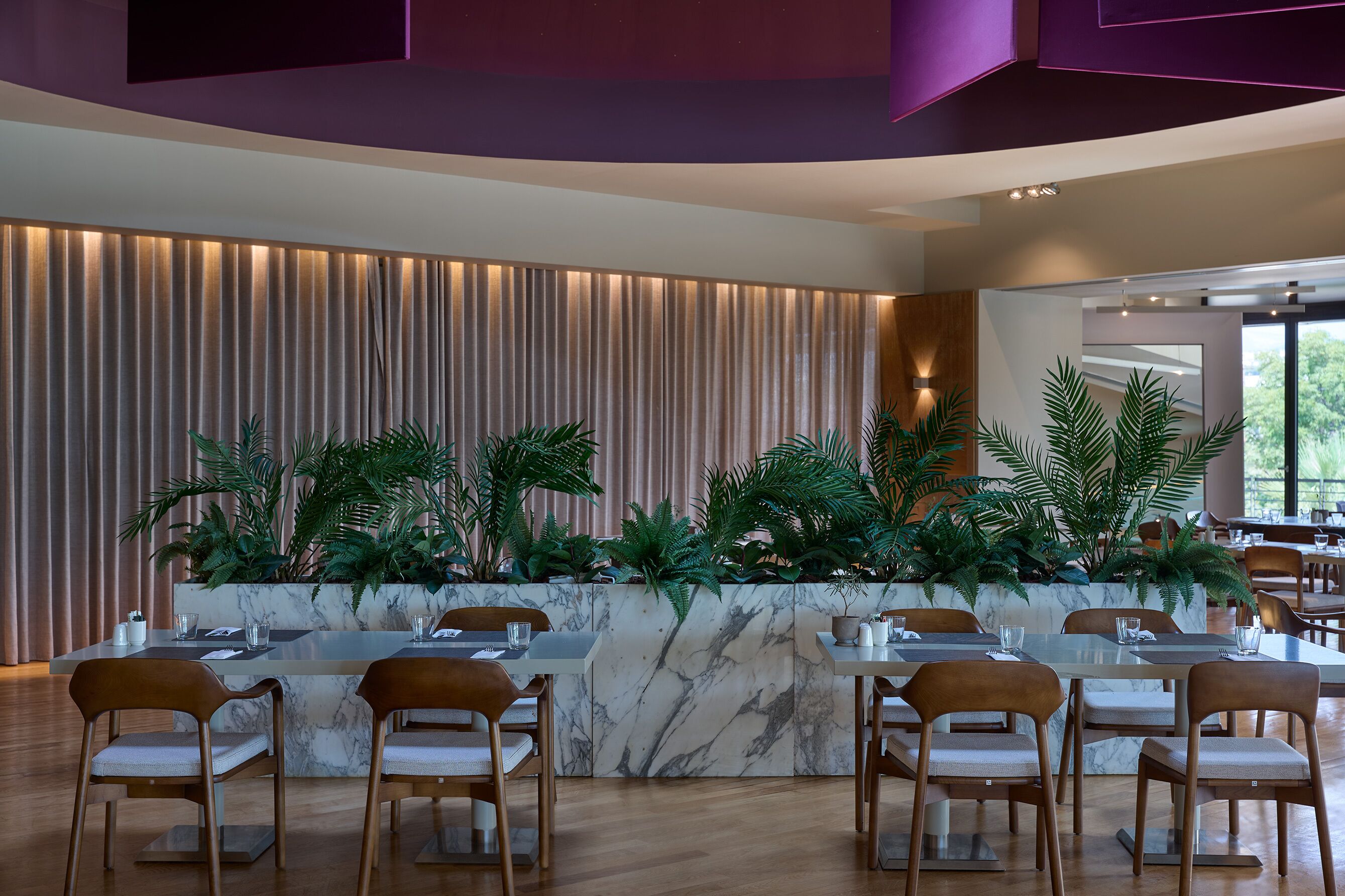 A modern dining area with a marble island, wooden chairs, and potted plants.