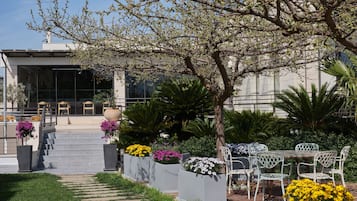 Un jardín con un sendero que conduce a una zona de estar con sillas y mesas, rodeado de plantas y flores.
