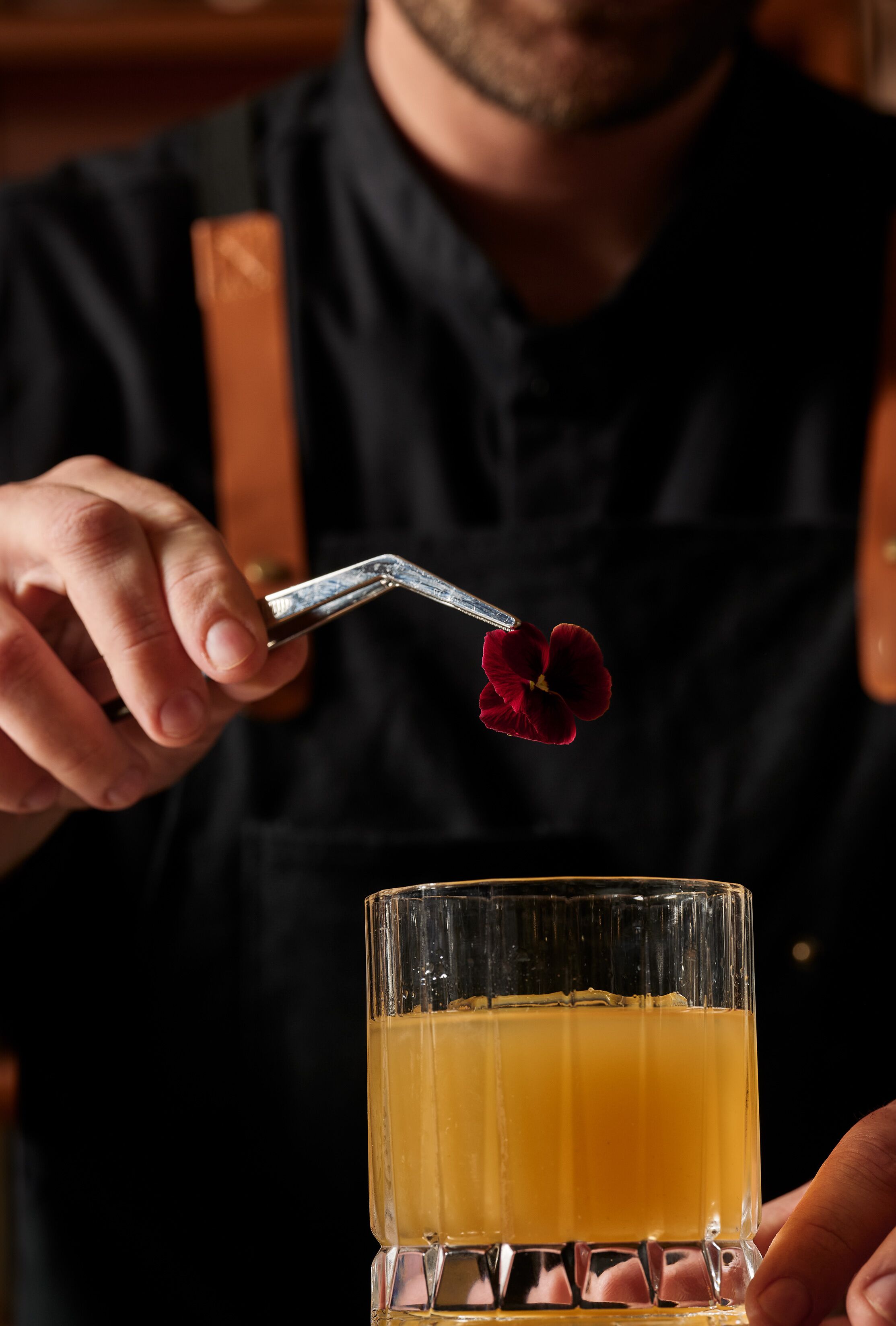 Uma pessoa segurando uma flor sobre um copo de líquido âmbar.