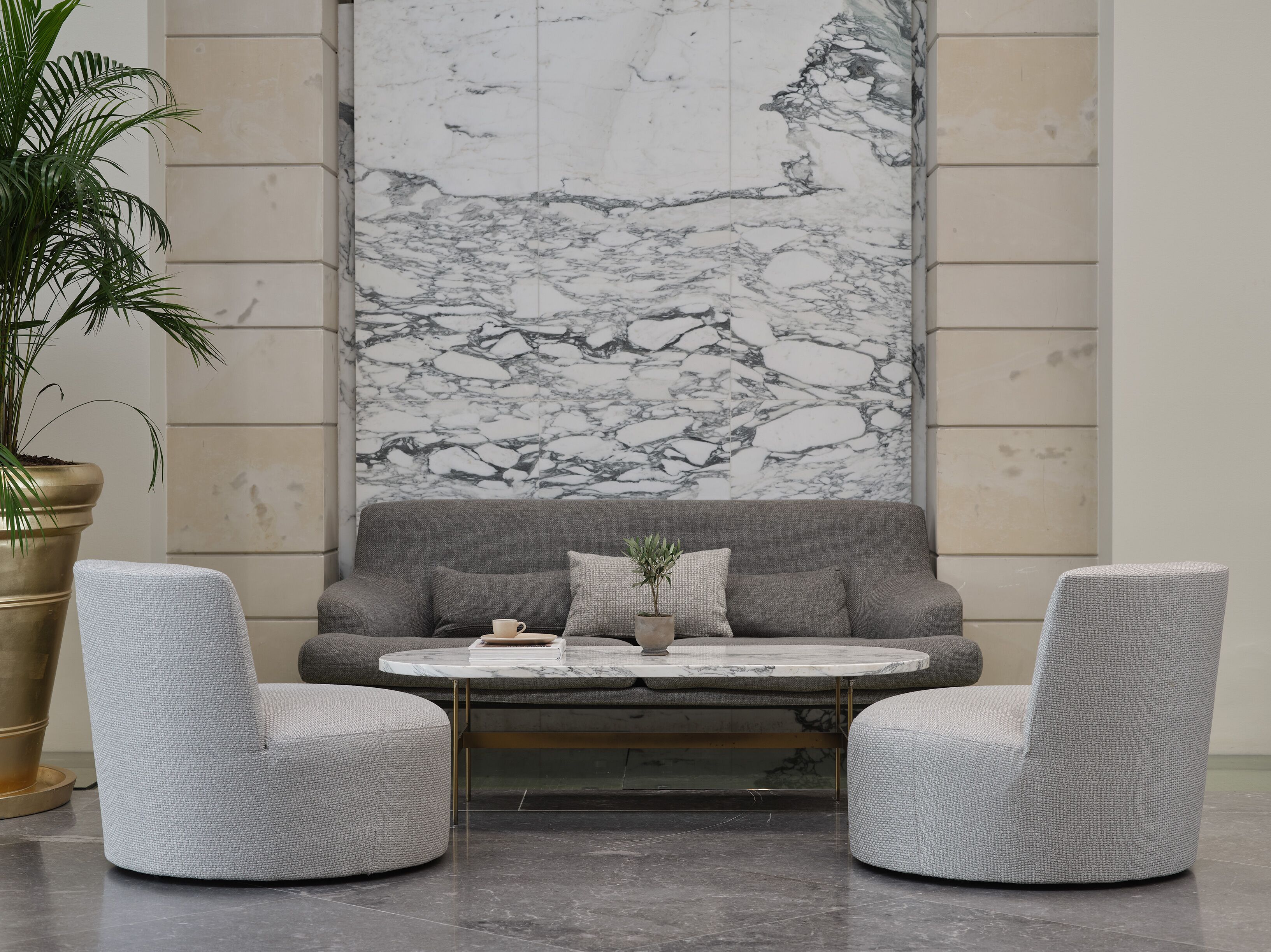 A modern lounge area with a marble wall, grey sofa, two armchairs, and a coffee table.