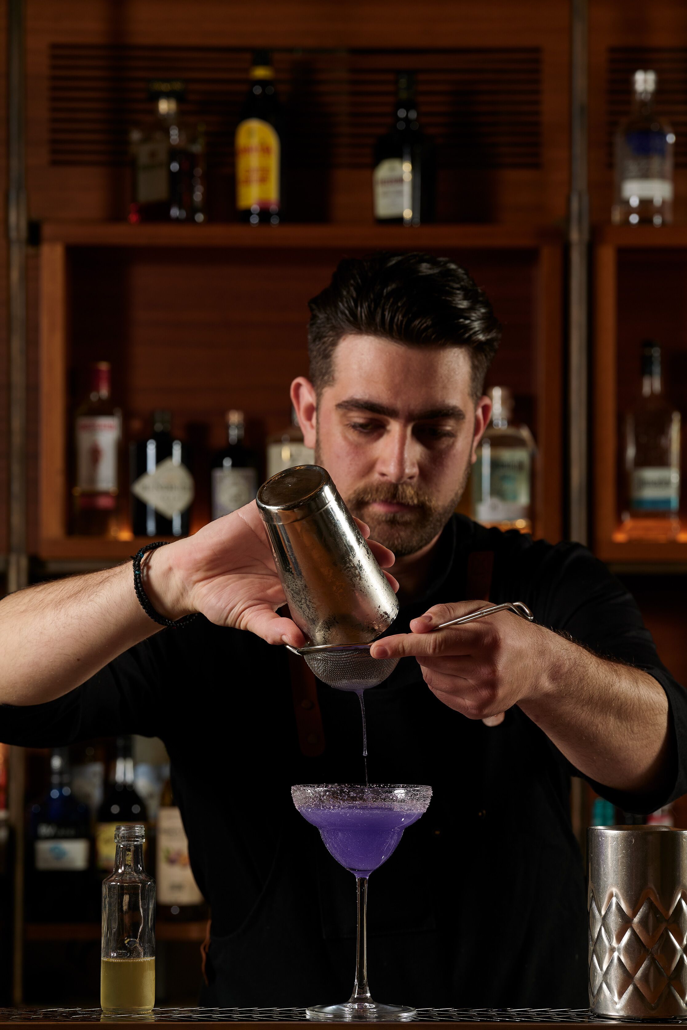 Ein Barkeeper gießt ein Getränk in ein Martini-Glas ein.