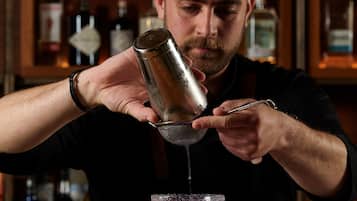 Ein Barkeeper gießt ein Getränk in ein Martini-Glas ein.