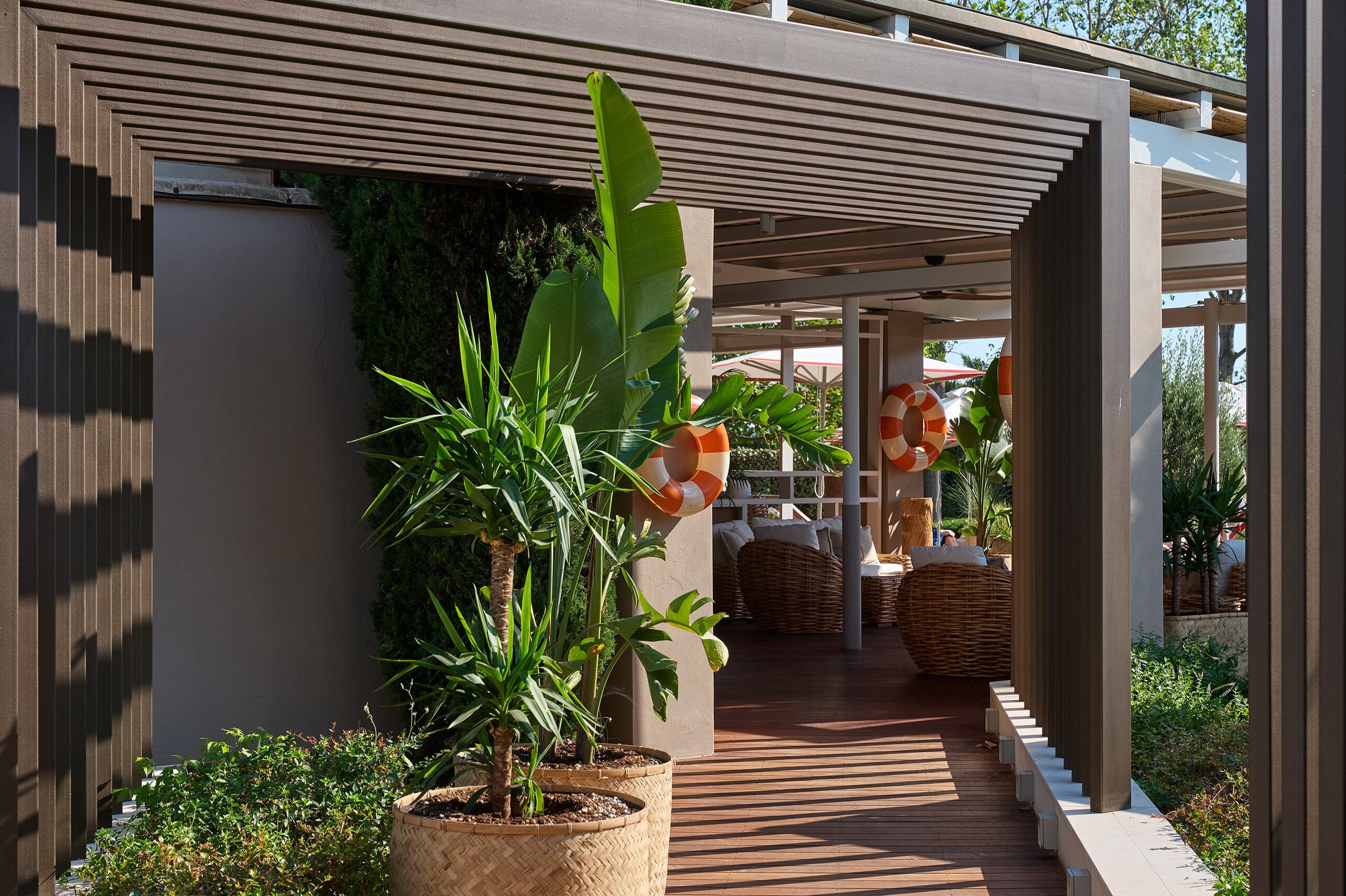 Uma área externa moderna com deck de madeira, plantas em vasos e um espaço de estar coberto com móveis de vime.