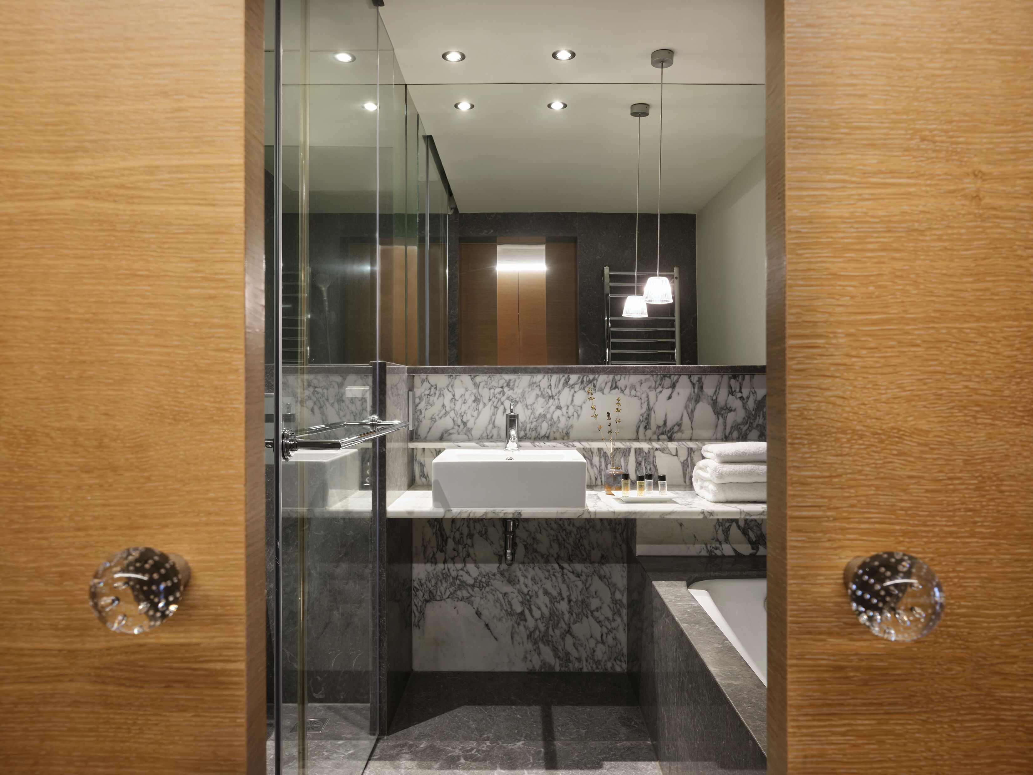 Une salle de bain moderne avec une douche à parois de verre, un lavabo blanc et un pare-baigneoire en marbre.