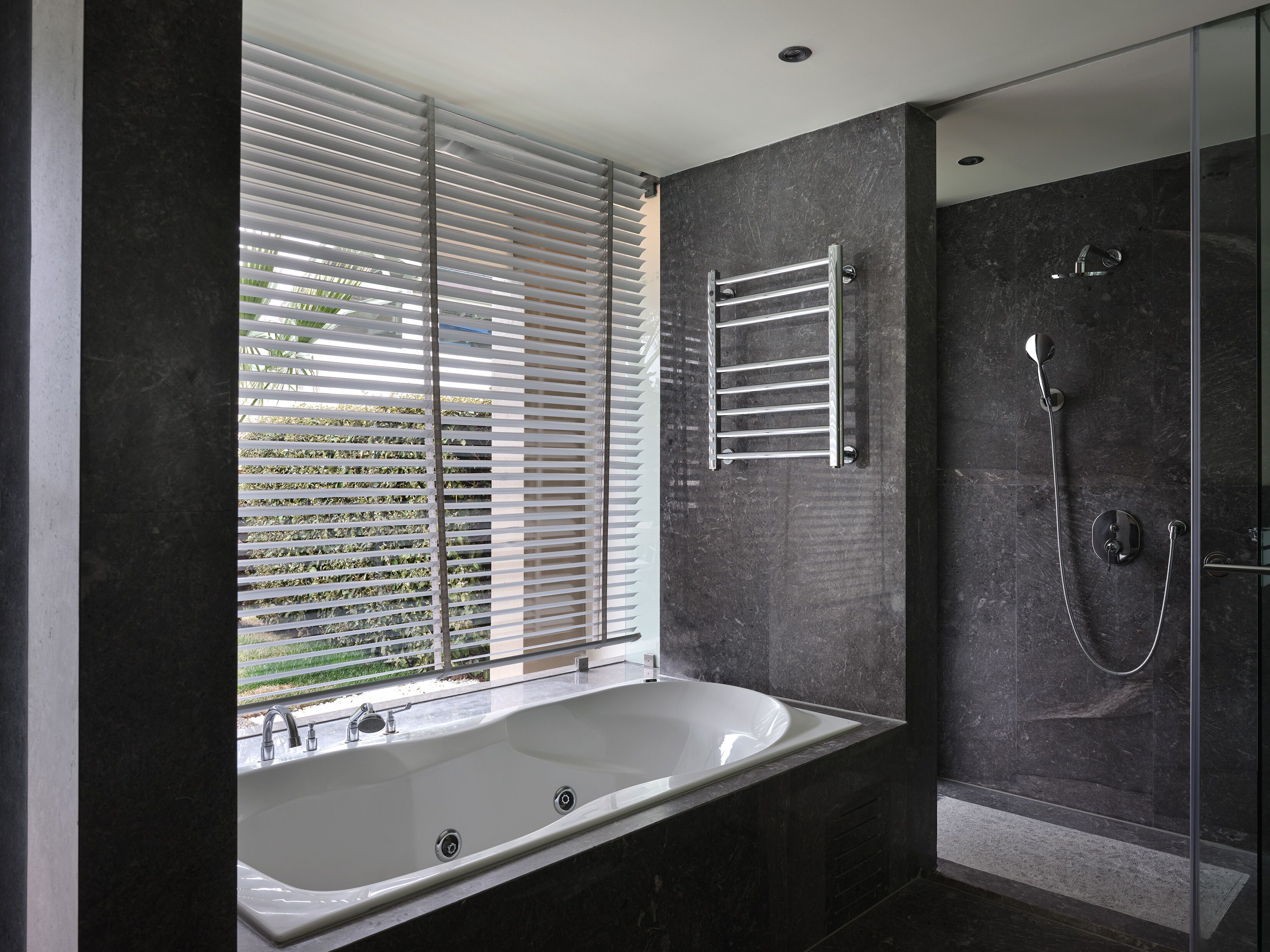 A modern bathroom with a large bathtub, a glass-enclosed shower, and a window with blinds.