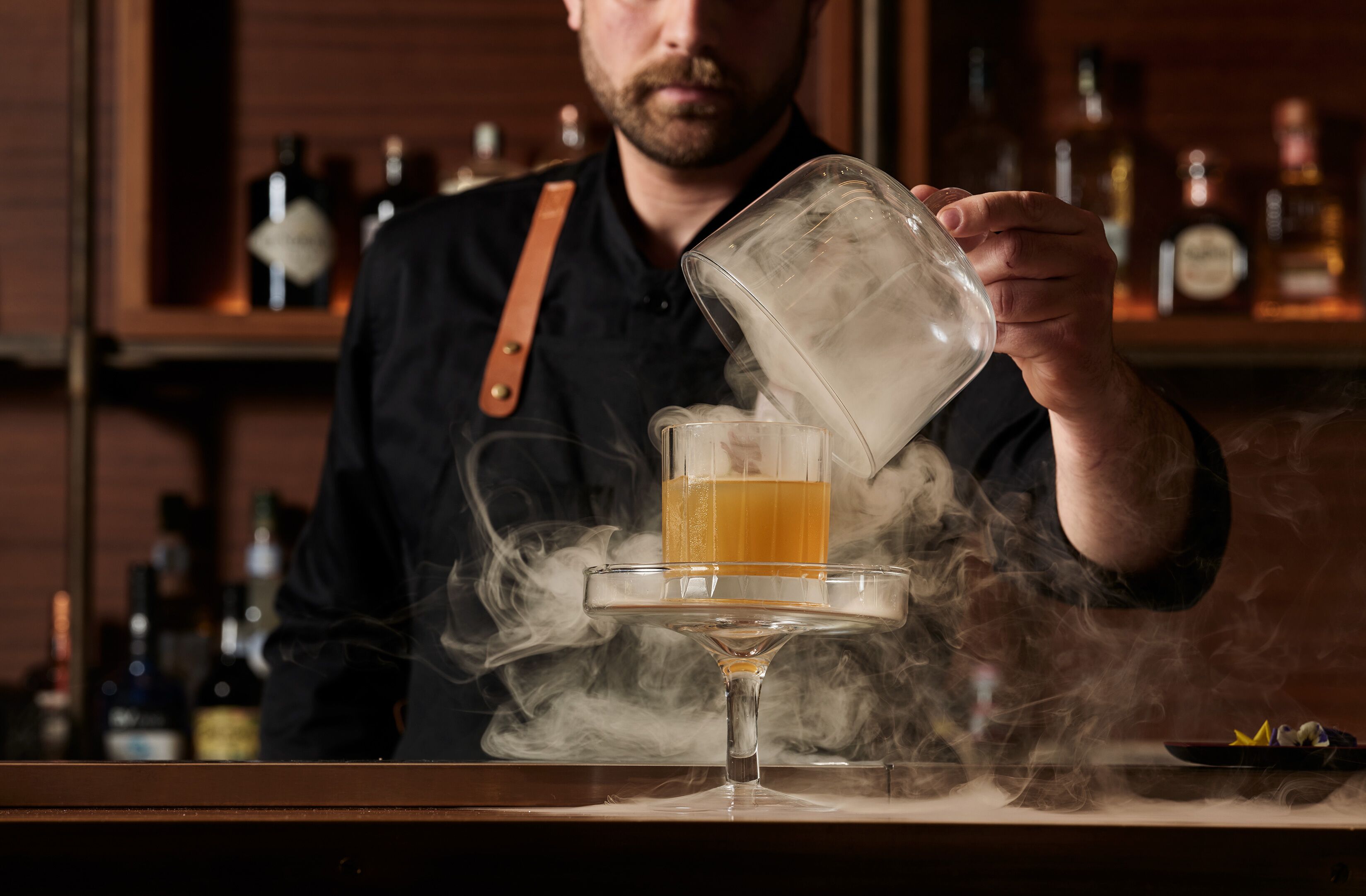 Um bartender servindo uma bebida em um copo com fumaça subindo.