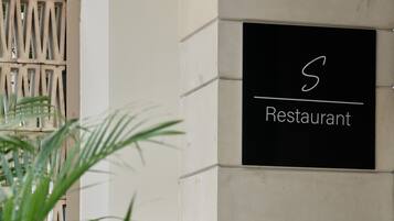 Un letrero de restaurante en la pared exterior de un edificio, una barandilla de metal y una planta en maceta.
