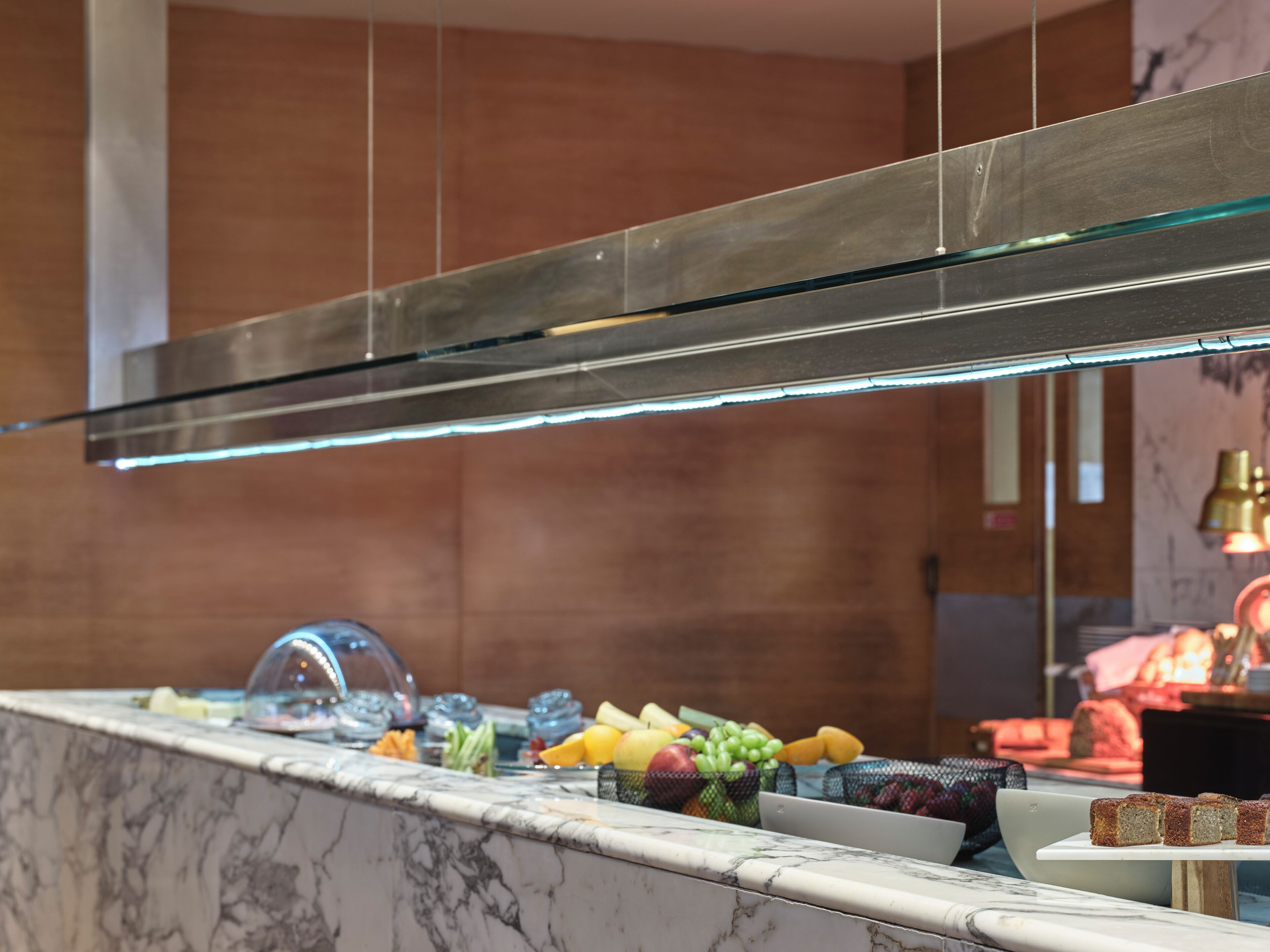 A marble countertop with a glass-top display case, a selection of fruits, and a slice of cake on a white plate.
