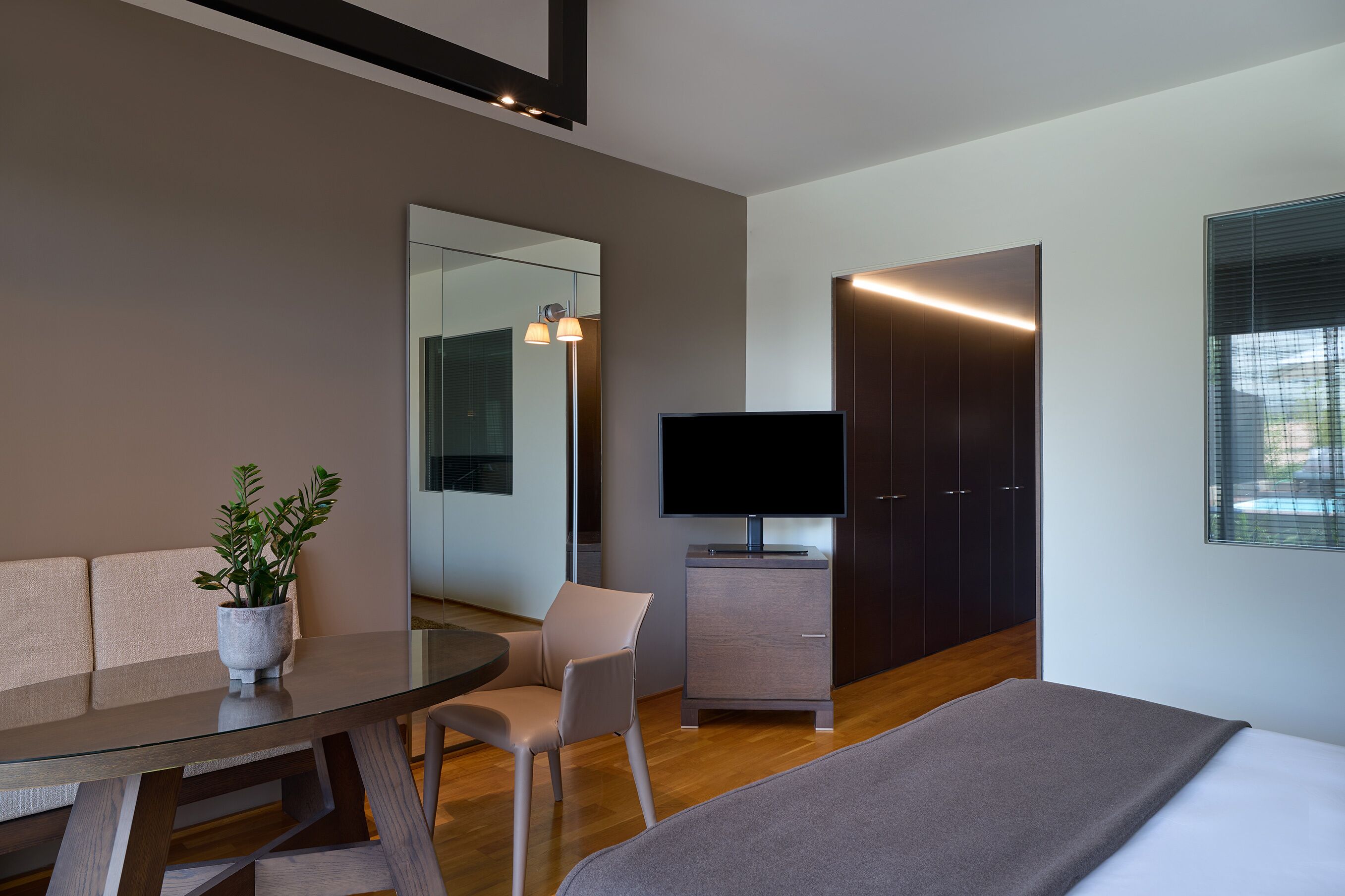 Una habitación de hotel moderna con sofá, mesa de comedor, televisor, armario y ventana.