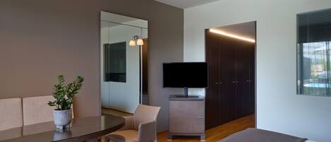 Una habitación de hotel moderna con sofá, mesa de comedor, televisor, armario y ventana.
