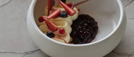 A white bowl with a dessert on a marble surface, a glass of water, and a spoon on a napkin.