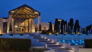 A modern hotel with a glass facade, a covered entrance, and a landscaped garden with a fountain. - September Hotel Thessaloniki (Pylaia-Chortiatis)