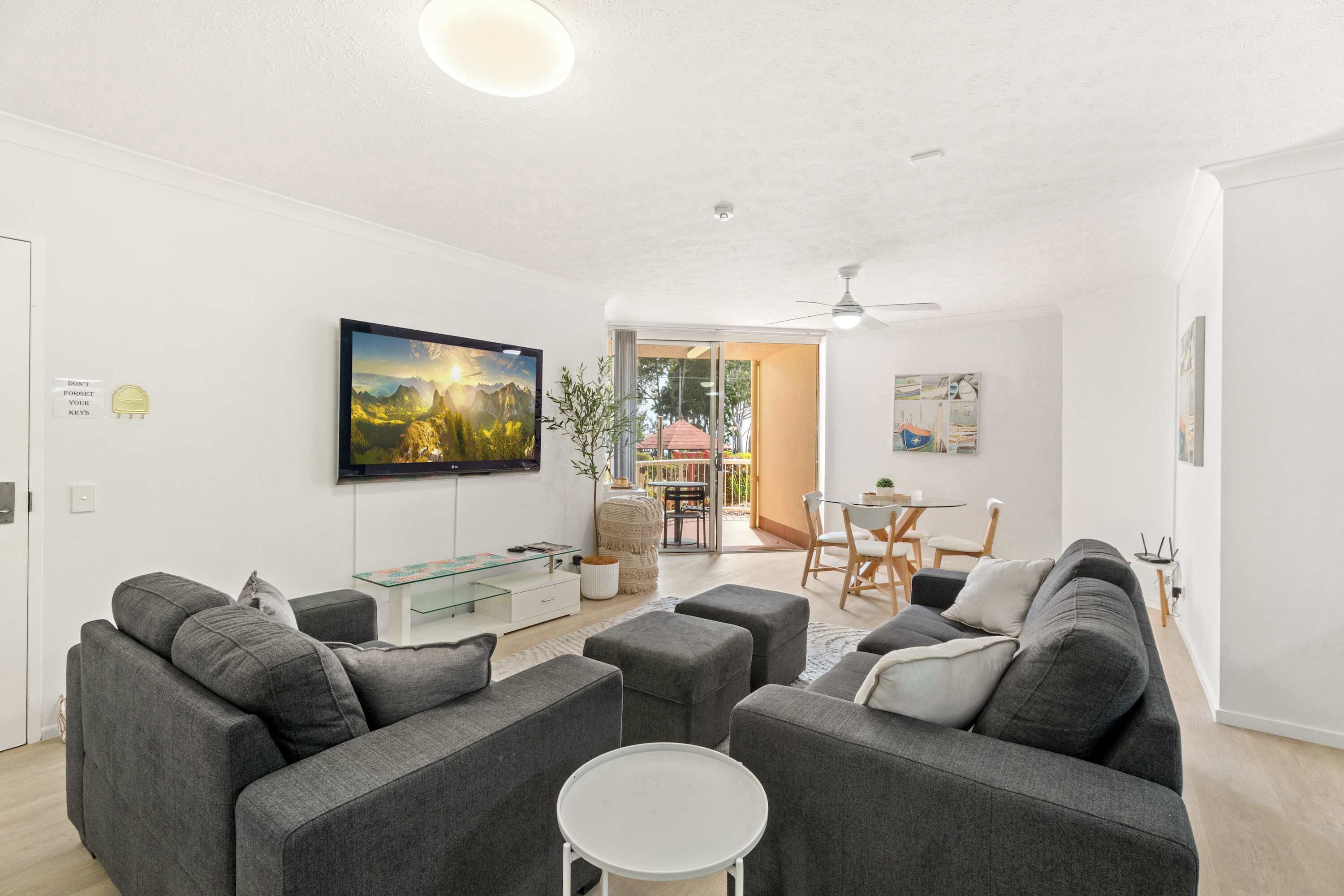 Een moderne woonkamer met grijze banken, een glazen salontafel en een flatscreen-tv aan de muur.