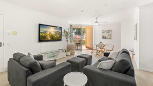 Een moderne woonkamer met grijze banken, een glazen salontafel en een flatscreen-tv aan de muur.