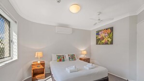 Ein Schlafzimmer mit einem großen Bett, zwei Nachttischen mit Lampen, einem Deckenventilator, einem Fenster mit Blick und einem Blumenbild an der Wand.