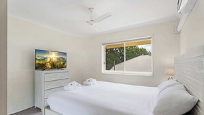 Un dormitorio con cama, televisión sobre una cómoda, ventana con vistas y ventilador de techo.