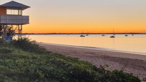 Una torre de salvavidas con vista a una playa tranquila y varios barcos en el agua al atardecer.