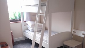 Ein Schlafraum mit Etagenbetten, einem Fenster, einem Stuhl und einem kleinen Tisch.