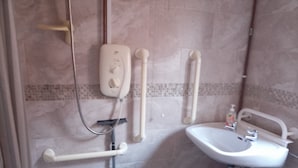 Ein Badezimmer mit einem weißen Waschbecken, einer Duschbrause, einer wandmontierten Toilette und Haltegriffen.