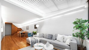 Una sala de estar moderna con un sofá gris, piso de madera y una escalera que sube a un nivel superior.