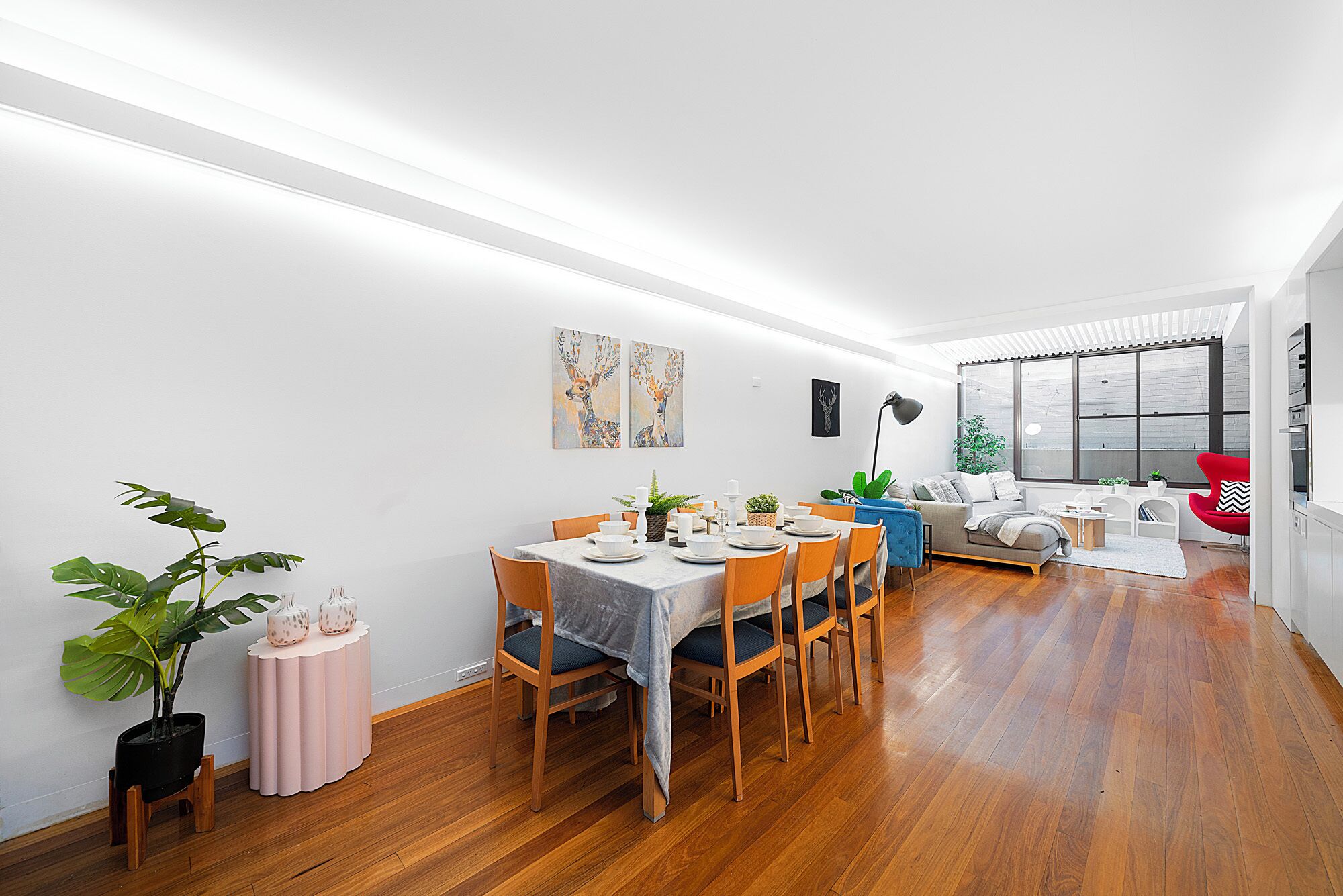 A modern dining area with a wooden floor, a dining table set for six, and a seating arrangement that includes a sofa and chairs.