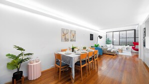 Un comedor moderno con suelo de madera, una mesa de comedor preparada para seis personas y una disposición de asientos que incluye un sofá y sillas.