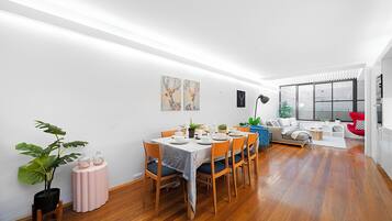 A modern dining area with a wooden floor, a dining table set for six, and a seating arrangement that includes a sofa and chairs.