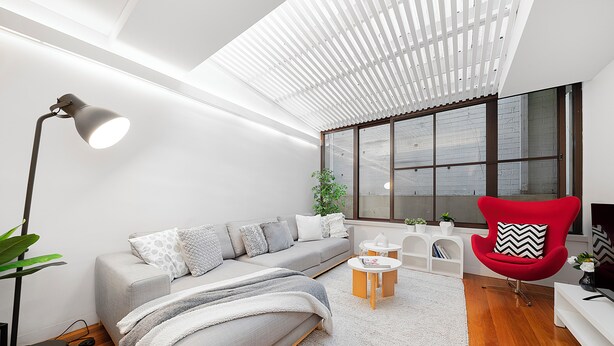 Una sala de estar moderna con un sofá gris, un sillón rojo, una lámpara de pie y un ventanal con vistas al exterior.