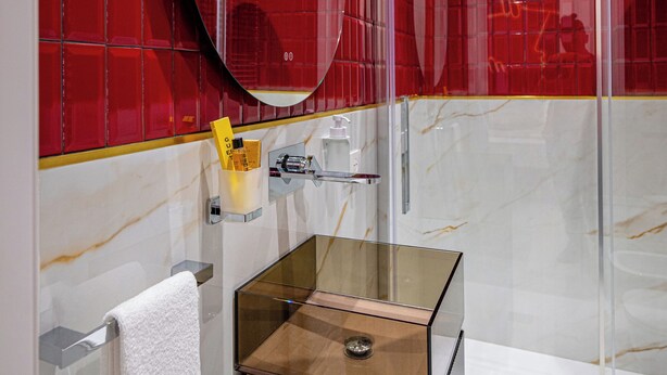 Een moderne badkamer met een douchecabine van glas, een rechthoekig wastafelmeubel met een marmeren blad en een rode betegelde wand.